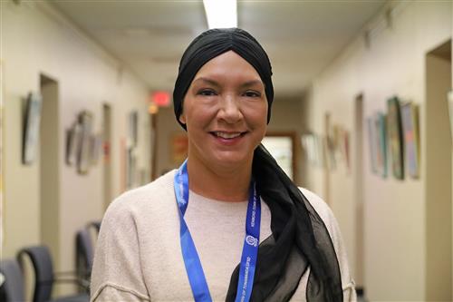 woman smiles at the camera wearing a white sweater and a black head scarf